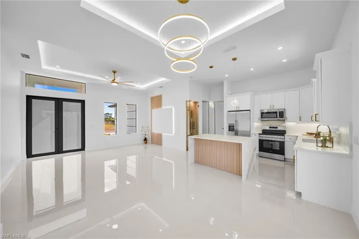 Kitchen with decorative light fixtures, white cabinetry, stainless steel appliances, a tray ceiling, and open floor plan