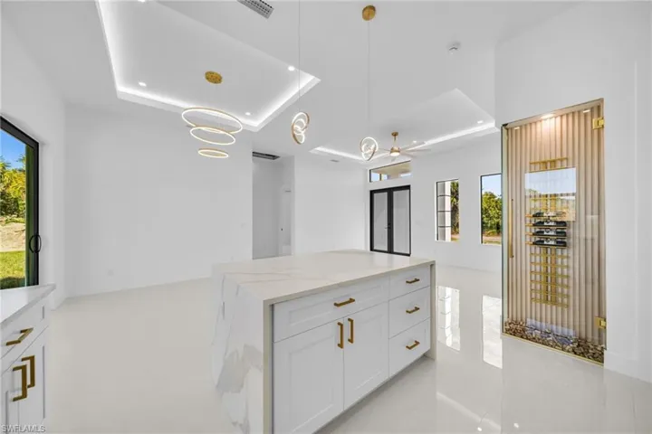 Kitchen featuring a raised ceiling, hanging light fixtures, white cabinetry, light stone counters, and a center island