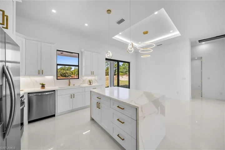 Kitchen featuring a raised ceiling, stainless steel appliances, white cabinets, a kitchen island, and light stone countertops