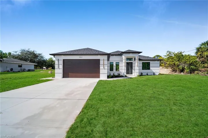 Prairie-style house with a front lawn, driveway, stucco siding, roof with shingles, and a garage