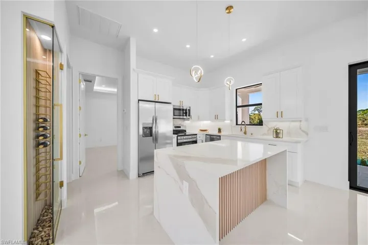 Kitchen featuring stainless steel appliances, a kitchen island, white cabinetry, light stone counters, and hanging light fixtures