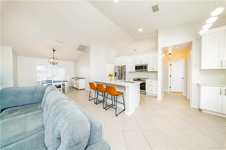 Kitchen with open floor plan, a kitchen bar, a kitchen island with sink, stainless steel appliances, and white cabinets