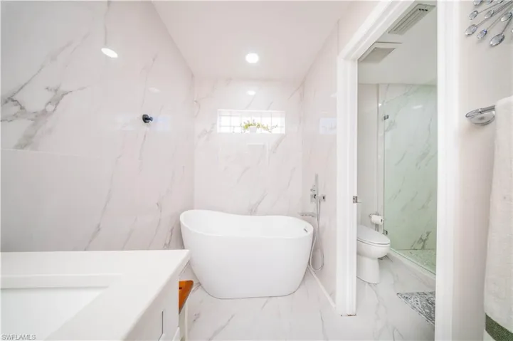 Full bathroom featuring vanity, a marble finish shower, stone wall, a freestanding bath, and recessed lighting