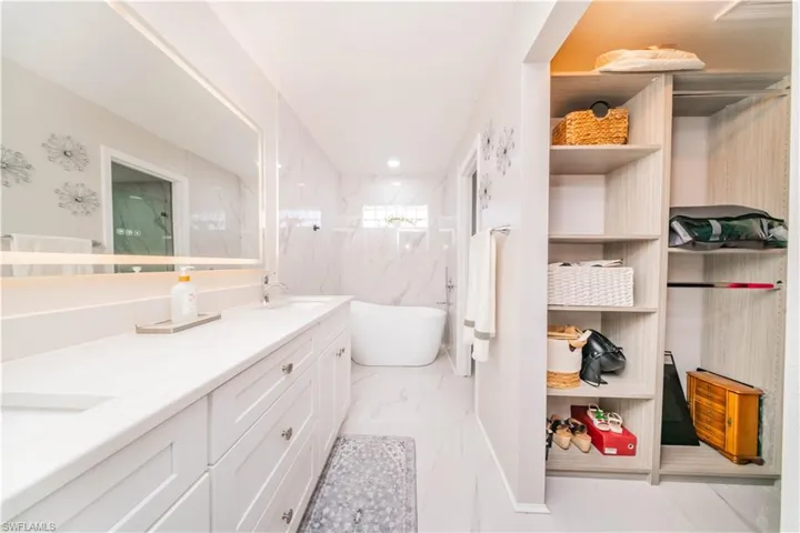 Bathroom with a freestanding tub, a marble finish shower, double vanity, light marble finish flooring, and recessed lighting