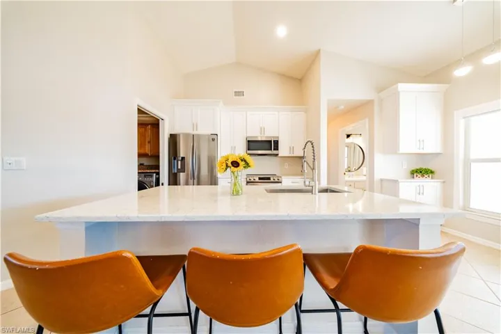 Kitchen with light tile patterned floors, stainless steel appliances, white cabinets, light stone counters, and lofted ceiling
