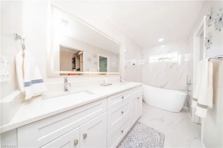 Bathroom featuring double vanity, a soaking tub, light marble finish flooring, and recessed lighting