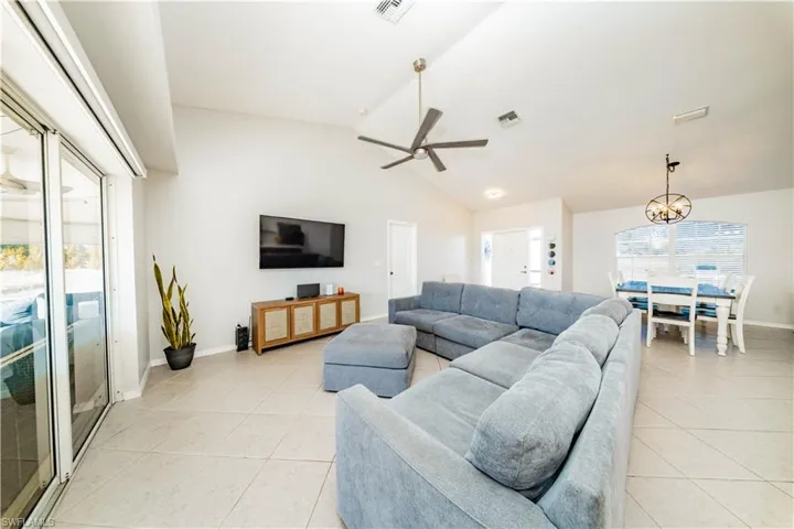 Living room with ceiling fan, lofted ceiling, hanging lights, and light tile patterned floors