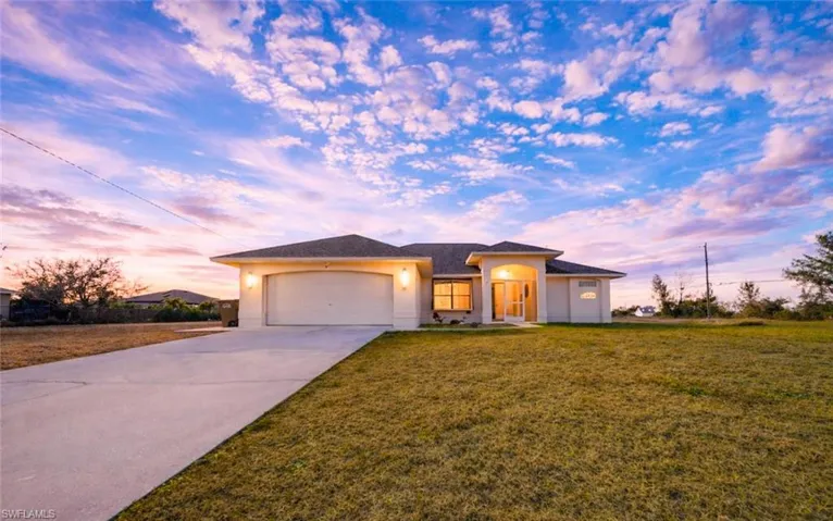 View of front of home with a yard, an attached garage, driveway, and stucco siding