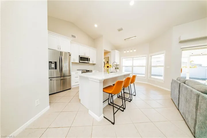 Kitchen featuring stainless steel appliances, white cabinetry, open floor plan, lofted ceiling, and a breakfast bar