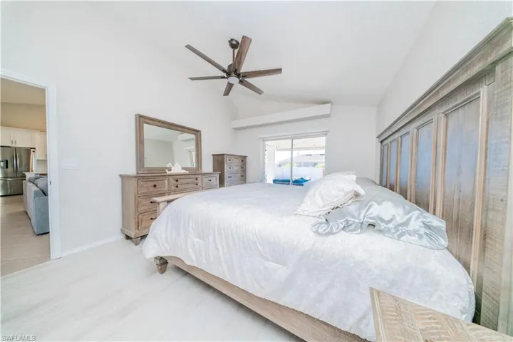 Bedroom with vaulted ceiling, stainless steel fridge, access to outside, ceiling fan, and wood finished floors