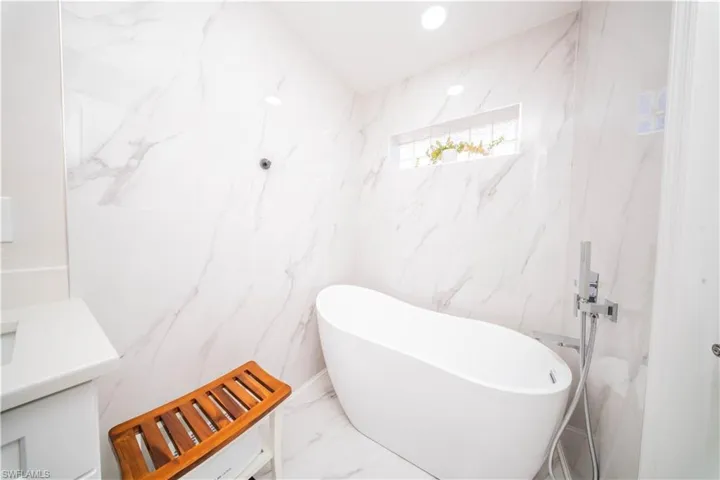 Full bath with vanity, stone wall, a soaking tub, recessed lighting, and marble tiled floors