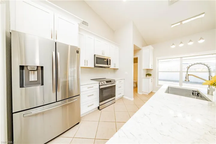 Kitchen featuring stainless steel appliances, white cabinets, light stone counters, lofted ceiling, and hanging light fixtures