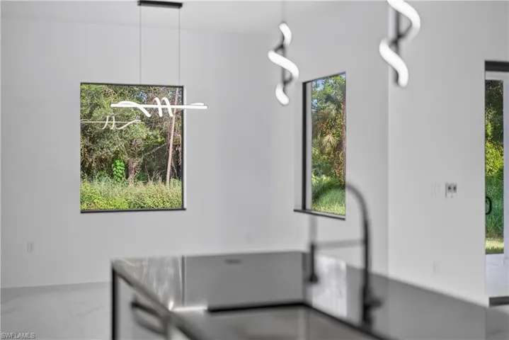 Modern pendant lighting, sleek black-framed windows, white interior walls, and a contemporary kitchen island with a black faucet