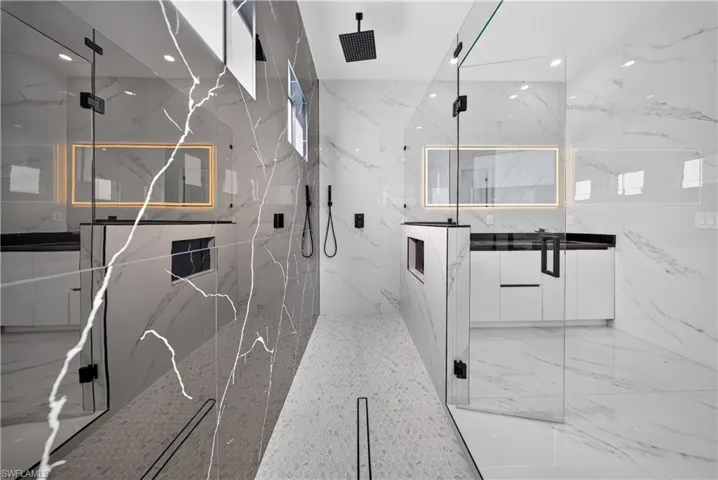 Dual walk-in shower with glass enclosures, marble-look tile, and matte black fixtures
