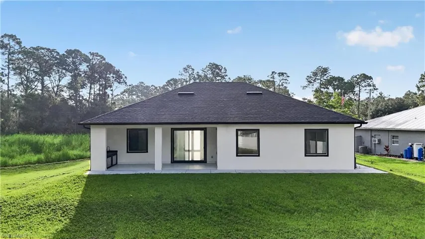 White stucco exterior with a dark shingle roof, covered patio with a built-in outdoor kitchen, and sliding glass doors
