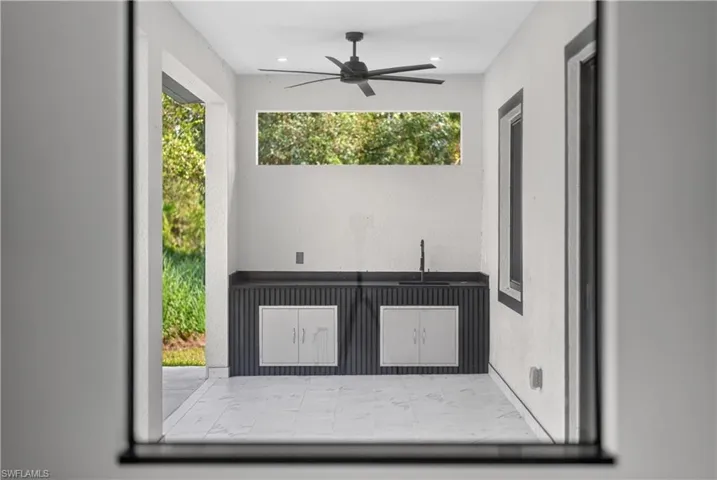 Outdoor kitchen space featuring a built-in sink, integrated cabinetry, dark countertop, and a ceiling fan