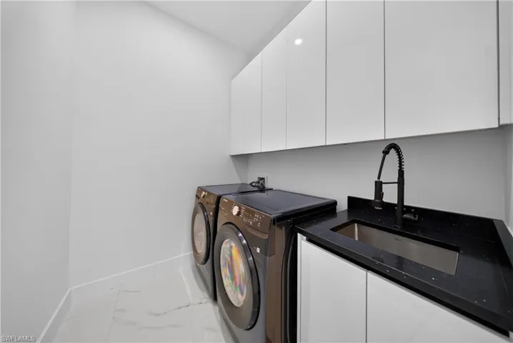 White upper and lower cabinetry, dark countertop with integrated sink, black pull-down faucet, and light-toned tile flooring