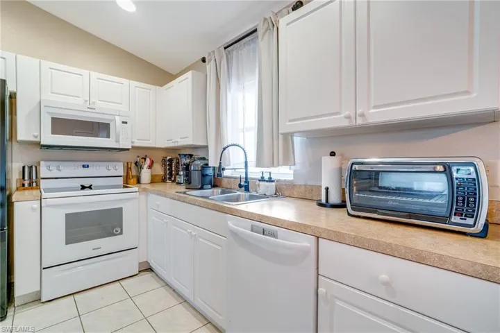 Kitchen featuring white appliances, light tile patterned floors, white cabinetry, and a sink