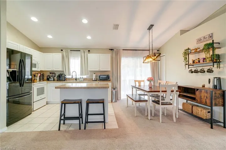 Kitchen featuring vaulted ceiling, light countertops, white appliances, and visible vents