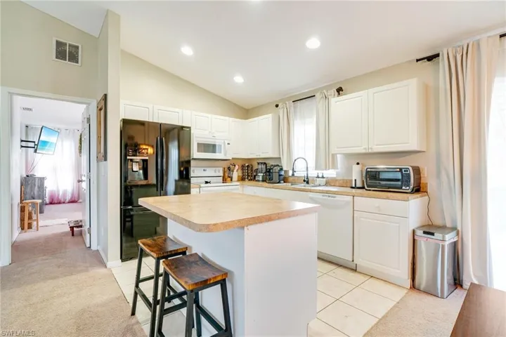 Kitchen featuring light carpet, white appliances, visible vents, and a sink