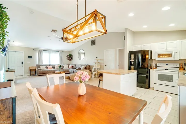 Dining area with lofted ceiling, light tile patterned floors, recessed lighting, light carpet, and an inviting chandelier