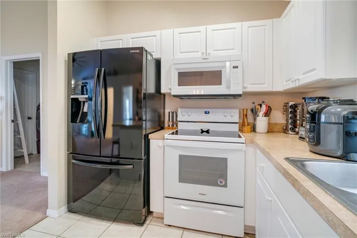 Kitchen with light tile patterned floors, light countertops, white appliances, and white cabinets