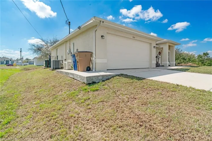 View of side of home with stucco siding, concrete driveway, a lawn, a garage, and cooling unit