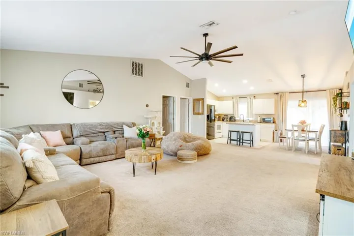 Living room featuring lofted ceiling, ceiling fan, visible vents, and light colored carpet