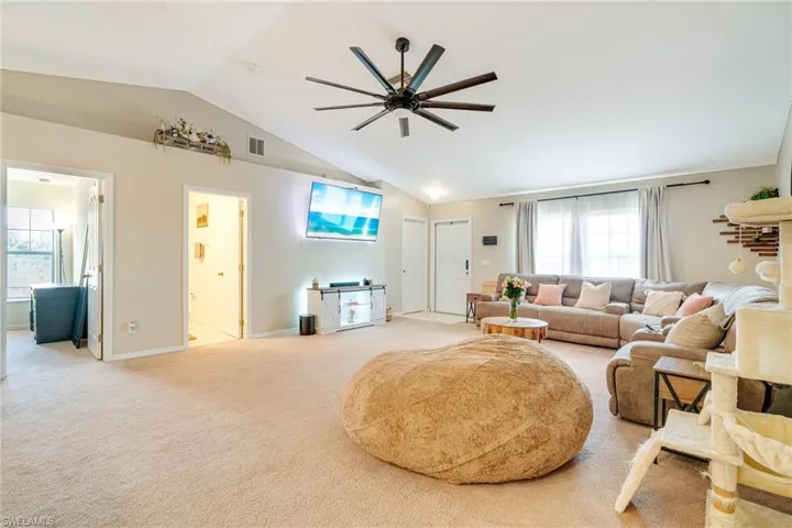 Living area with light carpet, baseboards, visible vents, a ceiling fan, and lofted ceiling