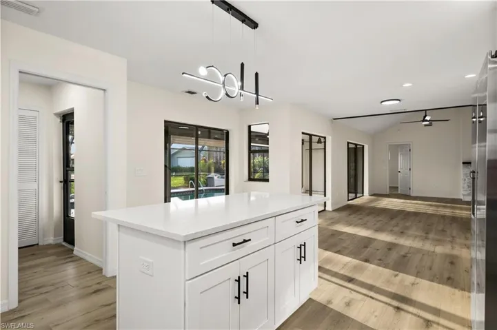 Kitchen with ceiling fan with notable chandelier, light hardwood / wood-style floors, lofted ceiling, and pendant lighting