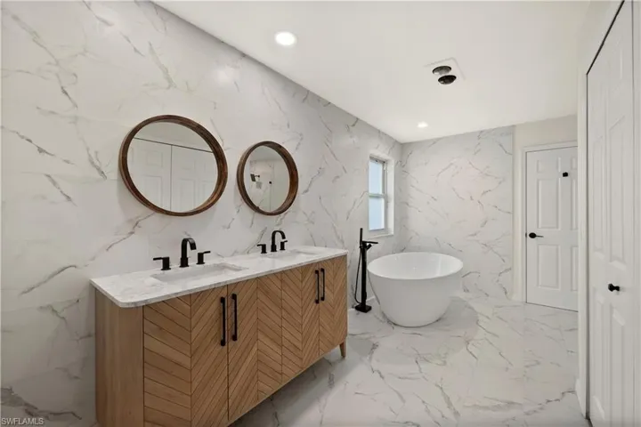 Bathroom with a bathtub, tile patterned flooring, dual bowl vanity, and tile walls