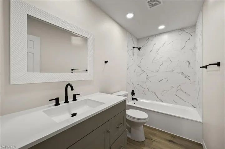 Full bathroom with vanity, toilet, tiled shower / bath, and hardwood / wood-style floors