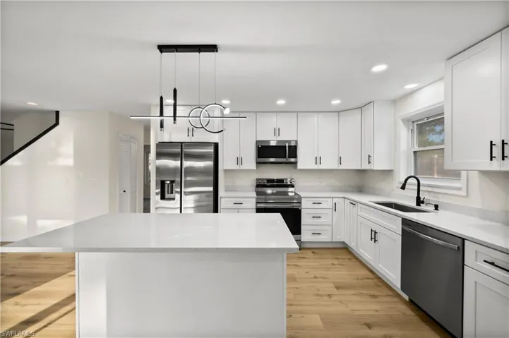 Kitchen with a kitchen island, stainless steel appliances, light hardwood / wood-style floors, decorative light fixtures, and sink