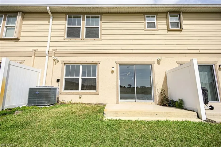 Rear view of house featuring stucco siding, cooling unit, fence, and a lawn