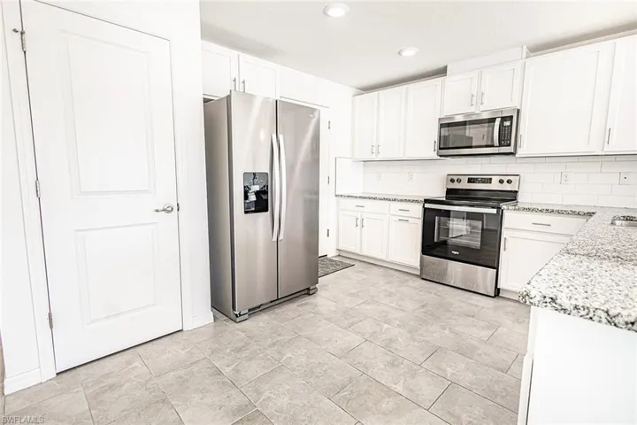 Kitchen featuring tasteful backsplash, white cabinets, appliances with stainless steel finishes, and light stone countertops