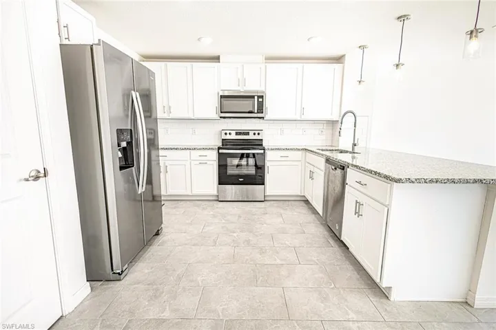 Kitchen with tasteful backsplash, a sink, appliances with stainless steel finishes, a peninsula, and light stone countertops