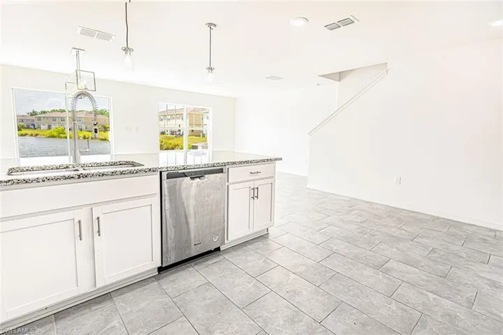 Kitchen featuring stainless steel dishwasher, a sink, white cabinetry, and visible vents