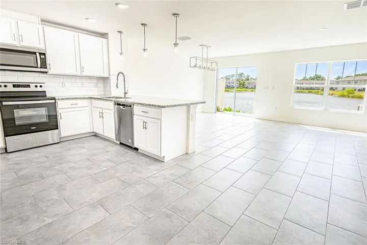 Kitchen featuring open floor plan, a peninsula, backsplash, light stone countertops, and appliances with stainless steel finishes