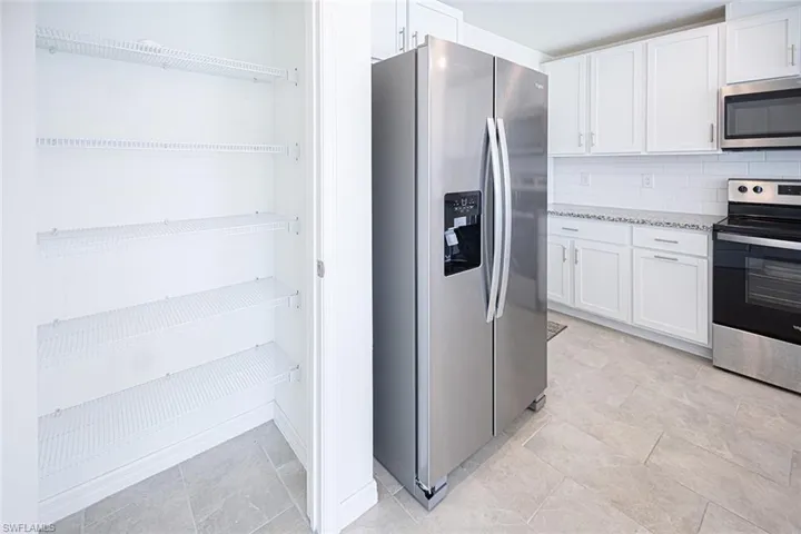 Kitchen with stainless steel appliances, tasteful backsplash, white cabinets, and light stone counters