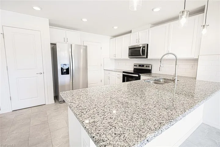 Kitchen with a peninsula, white cabinetry, light stone countertops, appliances with stainless steel finishes, and a sink