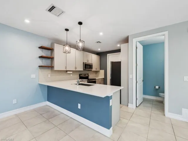 Kitchen with hanging light fixtures, stainless steel appliances, kitchen peninsula, and white cabinets