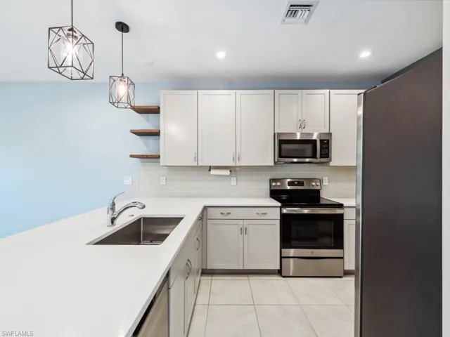 Kitchen featuring sink, white cabinetry, hanging light fixtures, light tile patterned floors, and stainless steel appliances