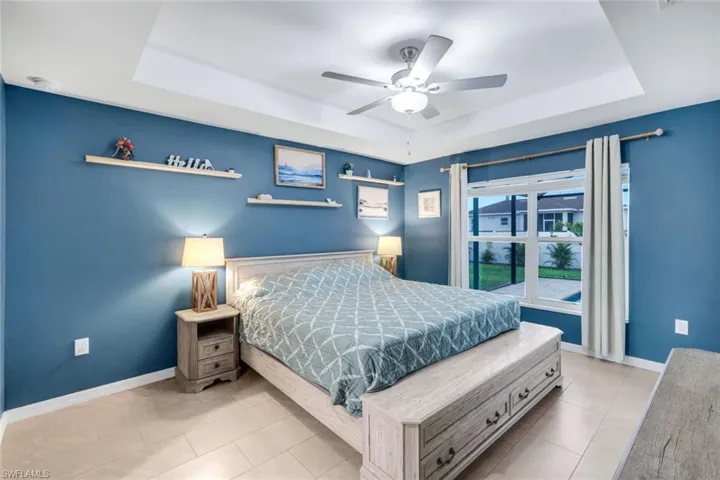 Bedroom featuring a tray ceiling, a ceiling fan, and light tile patterned floors