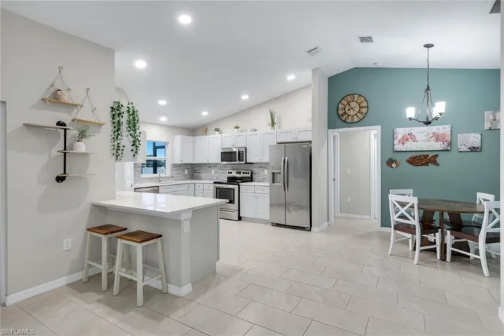 Kitchen featuring stainless steel appliances, open shelves, white cabinetry, lofted ceiling, and decorative backsplash