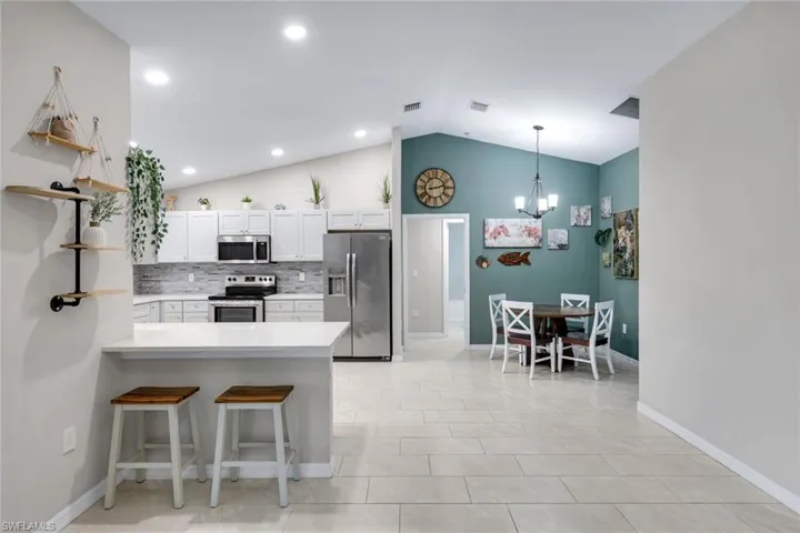 Kitchen with open shelves, a kitchen bar, stainless steel appliances, white cabinetry, and a peninsula