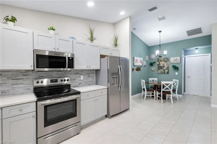 Kitchen with stainless steel appliances, lofted ceiling, light tile patterned floors, tasteful backsplash, and white cabinetry