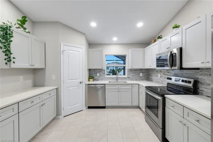 Kitchen featuring stainless steel appliances, decorative backsplash, recessed lighting, light stone counters, and white cabinetry