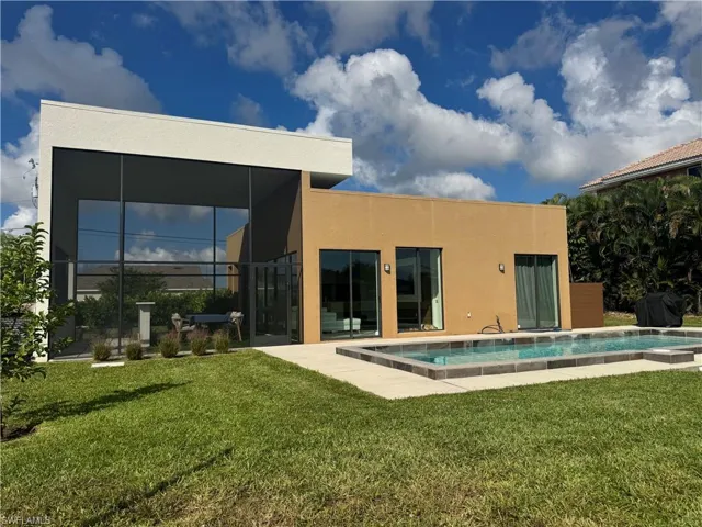 Rear view of property featuring a yard, a sunroom, an outdoor pool, and stucco siding