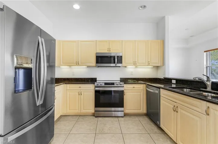 Kitchen featuring dark stone counters, appliances with stainless steel finishes, light tile patterned floors, and sink