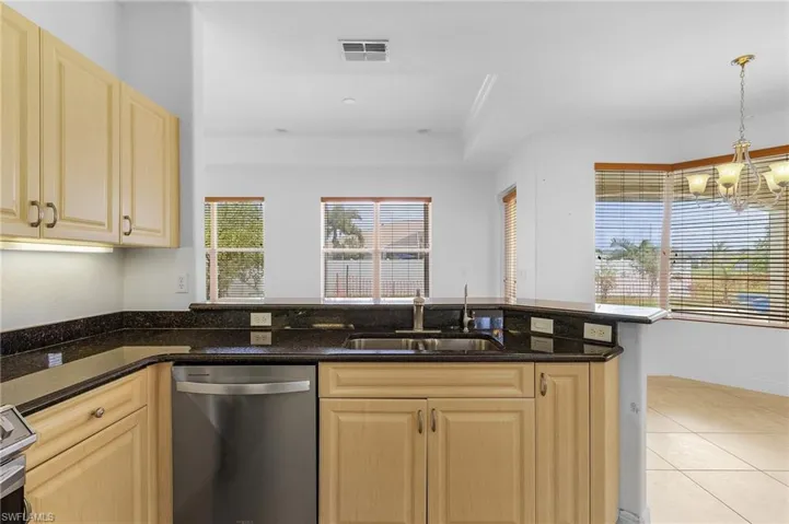 Kitchen featuring hanging light fixtures, sink, stainless steel appliances, dark stone countertops, and an inviting chandelier